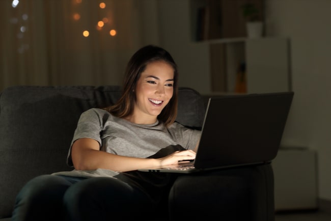 Glad tjej sitter i soffan med laptop i knät.